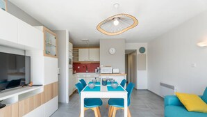 Une cuisine moderne avec des meubles blancs, une table à manger entourée de chaises bleues et un canapé bleu agrémenté d’un coussin jaune.
