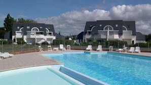 Une piscine avec des chaises longues et, en arrière-plan, un bâtiment à l’architecture moderne.