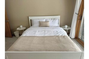 A neatly made bed with a checkered bedspread, two bedside tables with lamps, and a window with curtains.