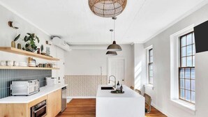 Ett modernt kök med träskåp, en vit bänkskiva och en köksö i mitten. Ovanför bänkskivan finns inbyggda hyllor och en hängande lampa.