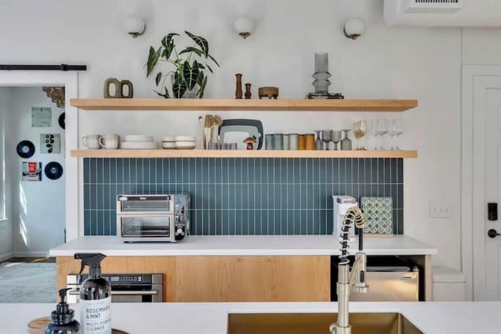 A modern kitchen with wooden shelves, a blue tiled backsplash, and a built-in oven.