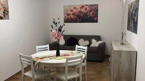 Ein Essbereich mit einem runden Tisch, weißen Stühlen, einer Blumenvase, einer Couch und einem Schrank.