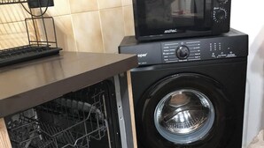 Eine kompakte Küche mit integrierter Waschmaschine und Trockner, einer Mikrowelle und einer kleinen Spüle.