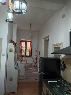 A kitchen with a stove, refrigerator, and hanging lights.
