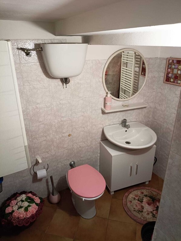 A bathroom with a toilet, sink, mirror, and a small shelf.