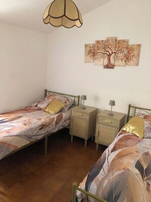 A bedroom with two single beds, a nightstand, a lamp, and a wall-mounted painting.