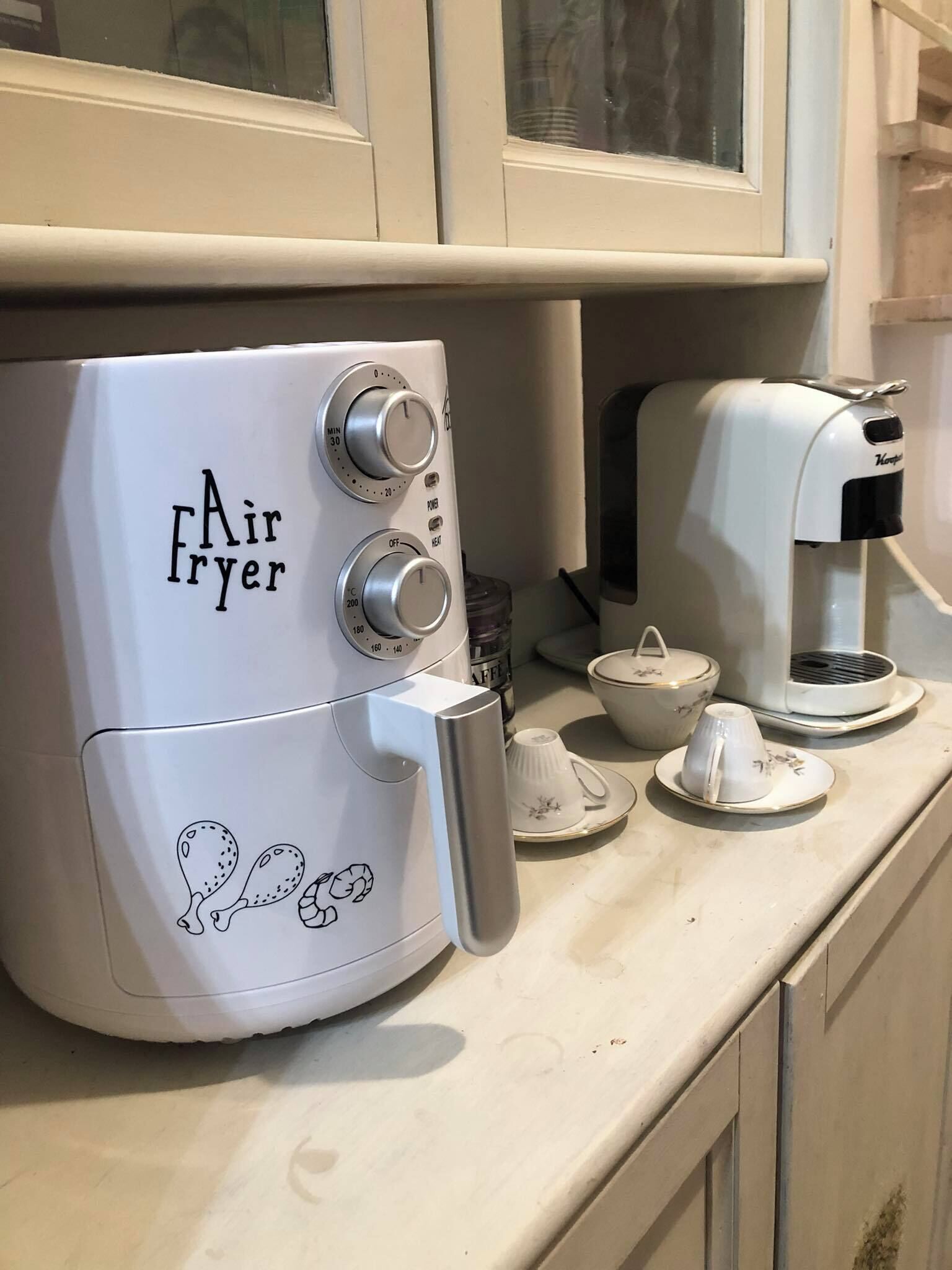Eine Küche mit einem Heißluftfritteuse, einer Kaffeemaschine und einem Tee-Set auf der Arbeitsfläche.