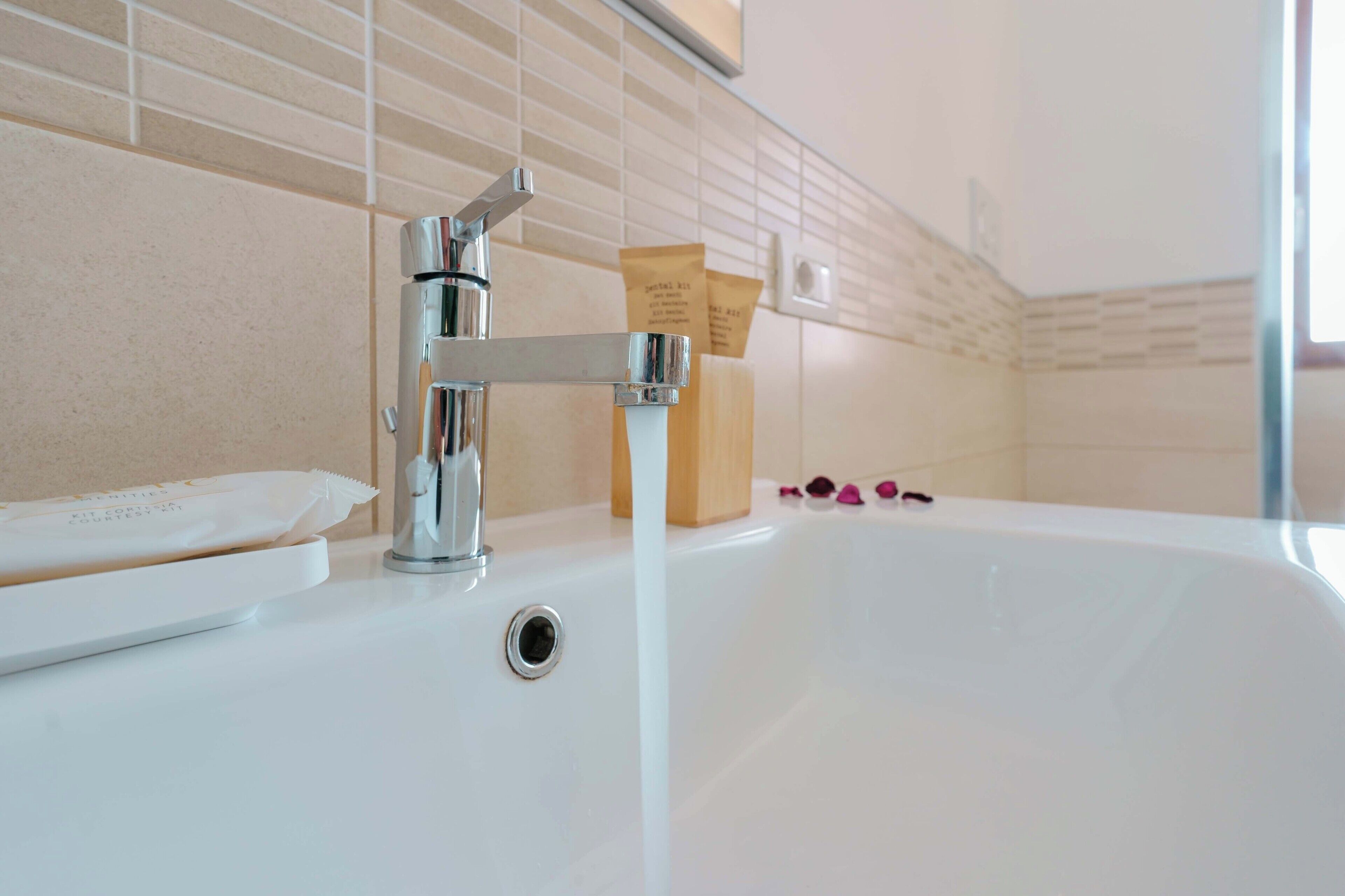 A bathroom with a white sink, chrome faucet, and a beige tiled wall.