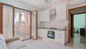 Une cuisine moderne avec des meubles blancs, un four encastré et une porte-fenêtre coulissante donnant sur un balcon.