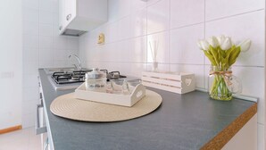 Une cuisine moderne avec des meubles blancs, une cuisinière à gaz et un vase décoratif contenant des fleurs blanches, posé sur le plan de travail.