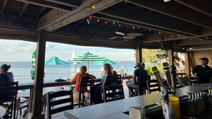 A restaurant with outdoor seating overlooking a body of water, featuring wooden beams, string lights, and umbrellas. - Most Beautiful View on Key West? (Key West)