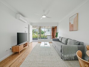 Una sala de estar moderna con un televisor de pantalla plana, un sofá gris, un mueble de entretenimiento de madera y un ventilador de techo.