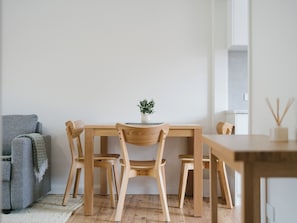 Un comedor minimalista con una mesa y sillas de madera, una pequeña planta en maceta y un sofá gris.