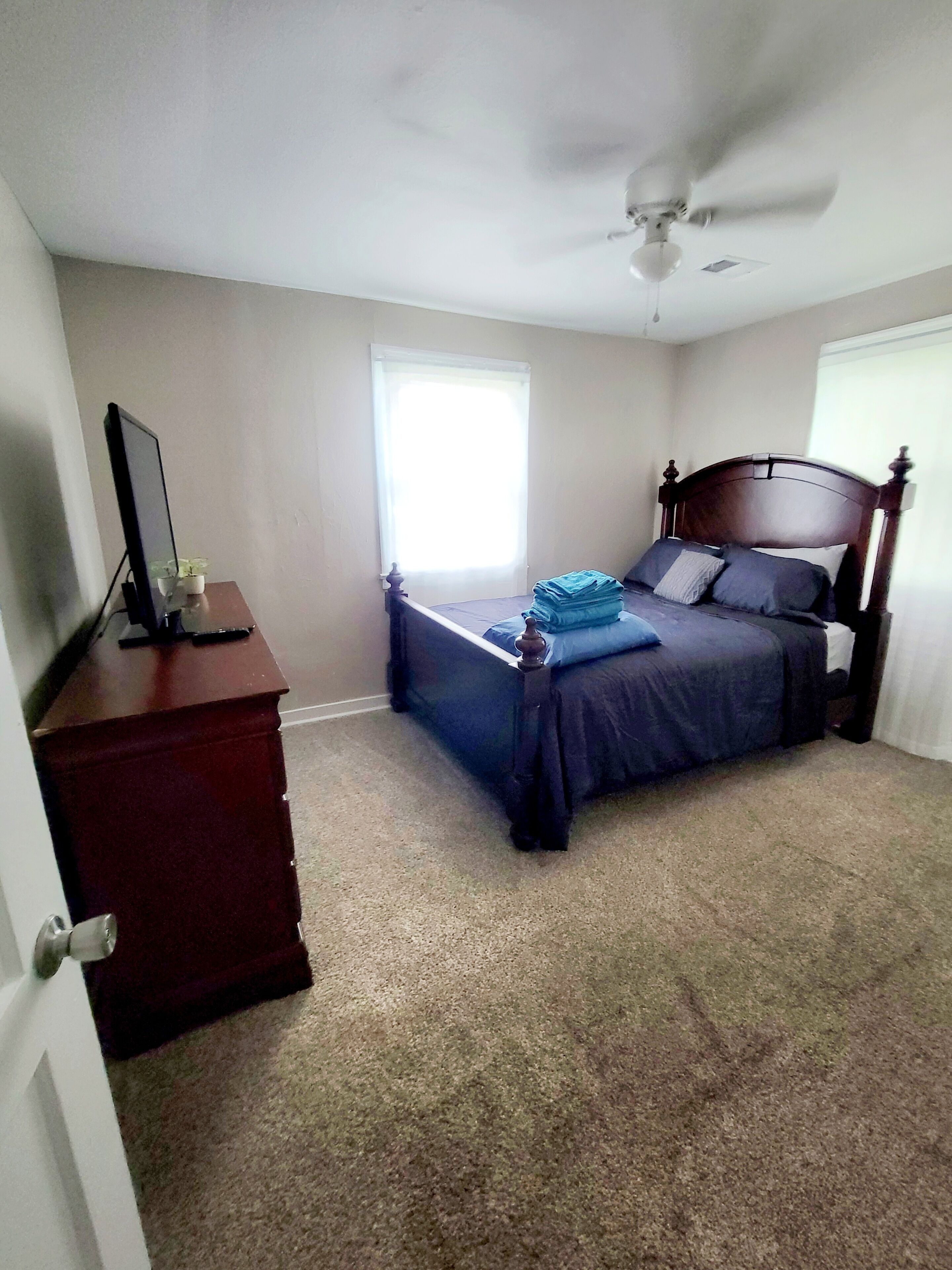 Quarto com cama, penteadeira, ventoinha no teto e janela.