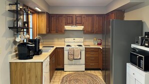 A compact kitchen with wooden cabinets, a white stove, a stainless steel refrigerator, and a coffee machine. - Cozy 3-bedroom house with a pool. Close to SPAC, Track and Downtown (Ballston Spa)