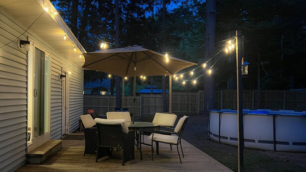 An outdoor deck with a table and chairs, string lights, and a covered area. - Cozy 3-bedroom house with a pool. Close to SPAC, Track and Downtown (Ballston Spa)