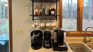 A kitchen with a coffee machine, a coffee maker, and a shelf with coffee bags and mugs. - Cozy 3-bedroom house with a pool. Close to SPAC, Track and Downtown (Ballston Spa)