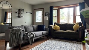 A living room with two sofas, a patterned rug, a large mirror, and a window with curtains. - Cozy 3-bedroom house with a pool. Close to SPAC, Track and Downtown (Ballston Spa)