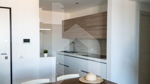 A modern kitchen with a glass countertop, wooden cabinets, and a dining area with a wooden table and chairs. - Homiday - OLYMPUS Seafront Luxury (Roseto degli Abruzzi)