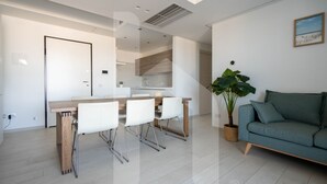 A modern living room with a sofa, a dining table with chairs, a kitchen area, and a large plant. - Homiday - OLYMPUS Seafront Luxury (Roseto degli Abruzzi)