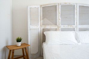 A bedroom with a bed, a wooden nightstand, and a potted plant.