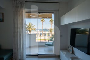 A room with a sliding glass door leading to a balcony with palm trees and a view of the sea.