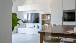 A modern kitchen with white cabinetry, a built-in oven, and a dining area with a wooden table and chairs. - Homiday - OLYMPUS Seafront Luxury (Roseto degli Abruzzi)