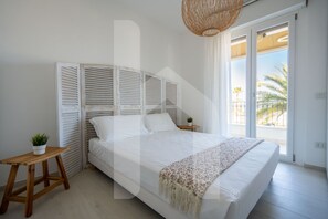 A bedroom with a large bed, a wooden nightstand, a potted plant, and a view of the outdoors through a sliding door.