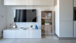 A modern kitchen with a built-in TV, white cabinetry, and a wooden shelf with decorative items. - Homiday - OLYMPUS Seafront Luxury (Roseto degli Abruzzi)