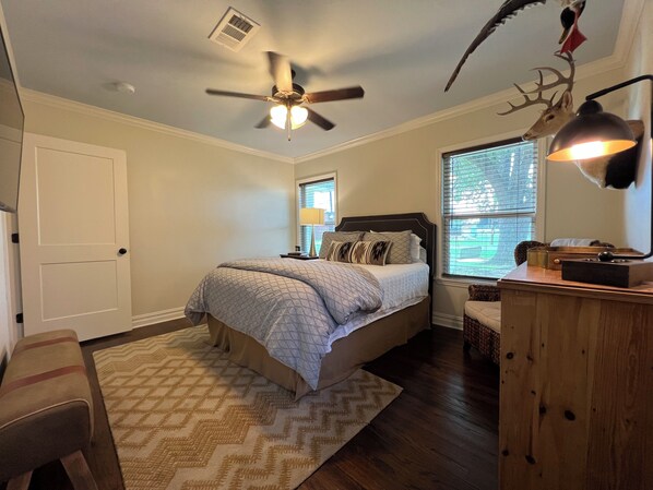 A bedroom with a bed, a ceiling fan, a window with blinds, a desk with a lamp, and a chair. - Stylish 3BR in Garden District near parks, river views, Neville High, and ULM. (Monroe)