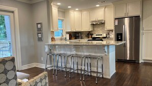 A modern kitchen with white cabinets, stainless steel appliances, and a central island with bar stools. - Stylish 3BR in Garden District near parks, river views, Neville High, and ULM. (Monroe)