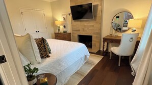 A hotel room with a bed, a desk, a chair, a TV, a fireplace, and a ceiling fan. - Stylish 3BR in Garden District near parks, river views, Neville High, and ULM. (Monroe)