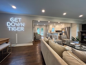 A modern living room with a sofa, a coffee table, and a neon sign reading "GET DOWN TIGER". - Stylish 3BR in Garden District near parks, river views, Neville High, and ULM. (Monroe)