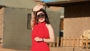 A person in a red dress kneeling on sandy ground with buildings in the background. - Room-wadi RUM Guide, Camp & Tour (Wadi Rum)