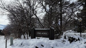 A sign for Pine Acres with a snow-covered landscape and trees in the background.