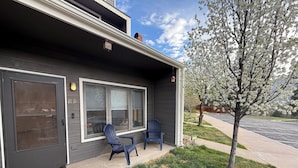 A residential house with a dark exterior, large windows, and a small porch with two chairs.