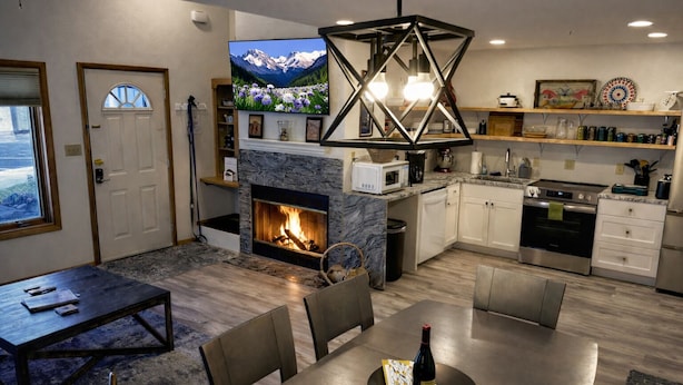 A modern living room with a fireplace, dining area, kitchen, and a TV mounted on the wall.