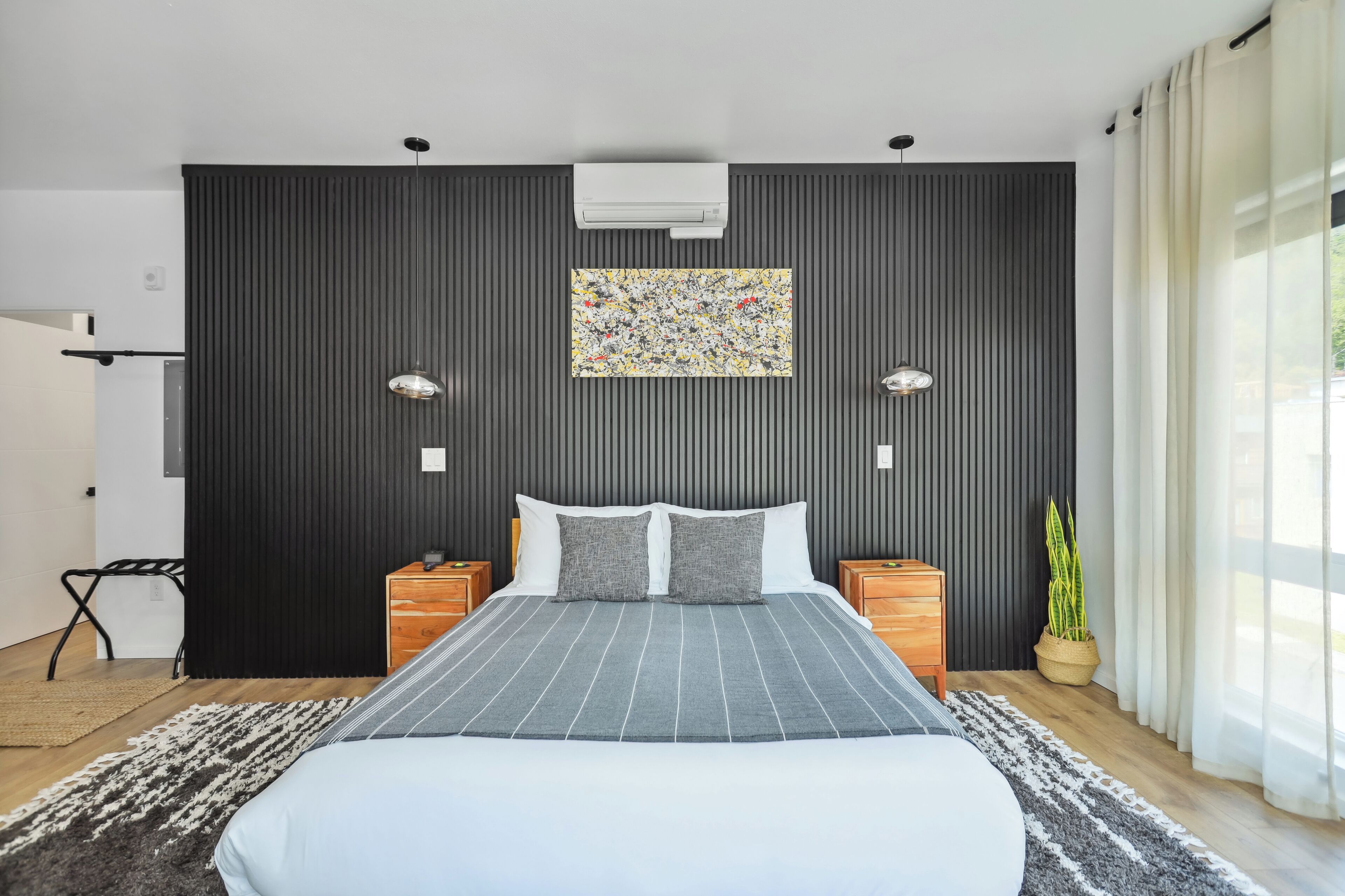 A modern bedroom with a large bed, two bedside tables, a wall-mounted air conditioner, and a potted plant.