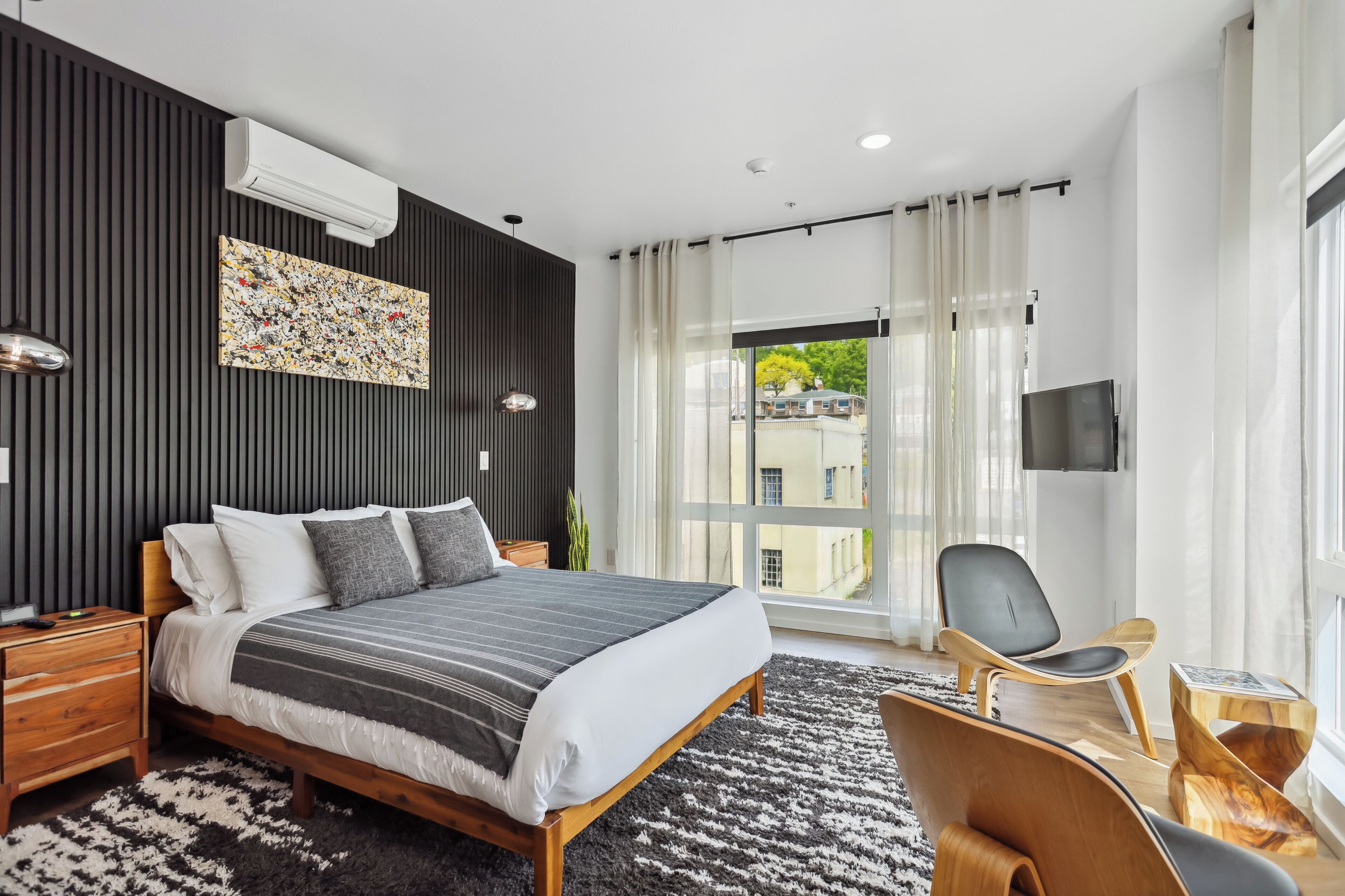 A modern bedroom with a large bed, a TV, and a view of the city.