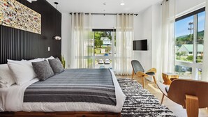 A modern bedroom with a large bed, a flat-screen TV, and a view of the street through sheer curtains. - Penthouse studio suite, downtown White Salmon, suite 15 (White Salmon)