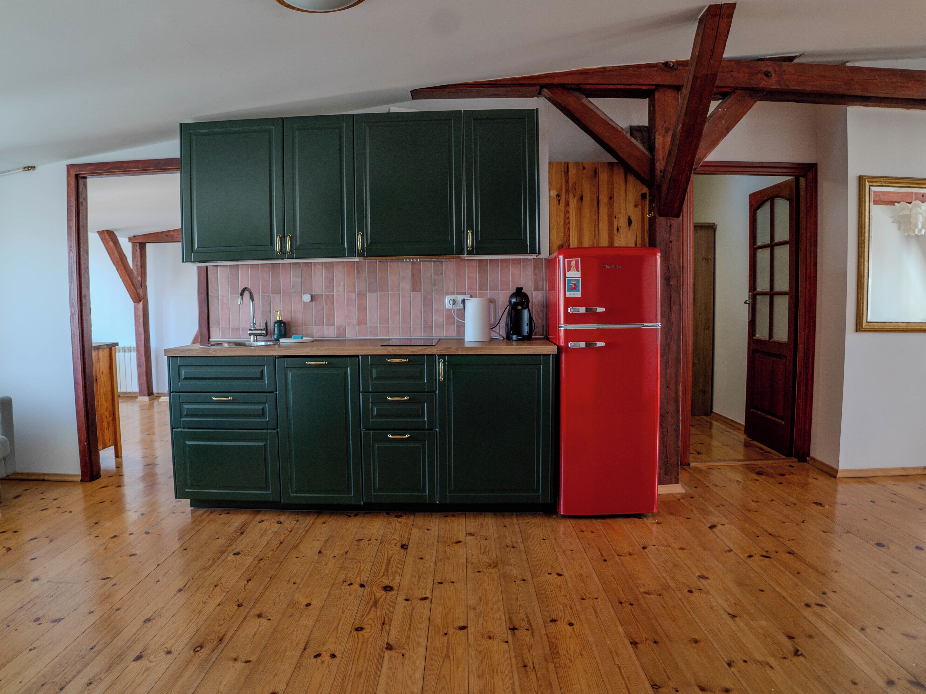 Eine Küche mit grünen Schränken, einem roten Kühlschrank, Holzbalken und einer gefliesten Spritzschutzwand.