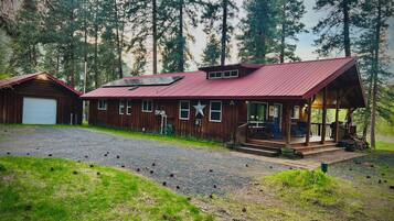 Escape to a secluded cabin surrounded by tall pine trees, with a spacious porch and a rustic red roof.