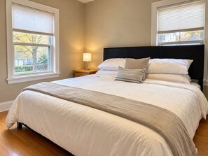 Une chambre avec un grand lit, deux tables de chevet et une fenêtre avec des stores.