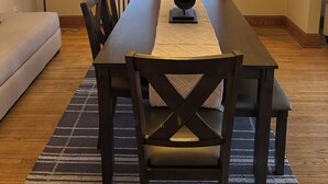 Een eethoek met een houten tafel, donkere stoelen, een kroonluchter en een raam met jaloezieën.