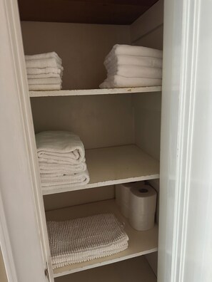 A storage closet with three shelves, each holding folded white towels.