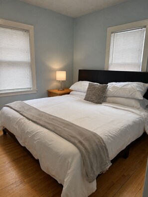 Une chambre à coucher avec un grand lit, deux tables de chevet, une lampe et une fenêtre avec des stores.
