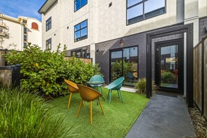 A modern building with a courtyard featuring artificial grass, a seating area with chairs, and a glass door entrance.