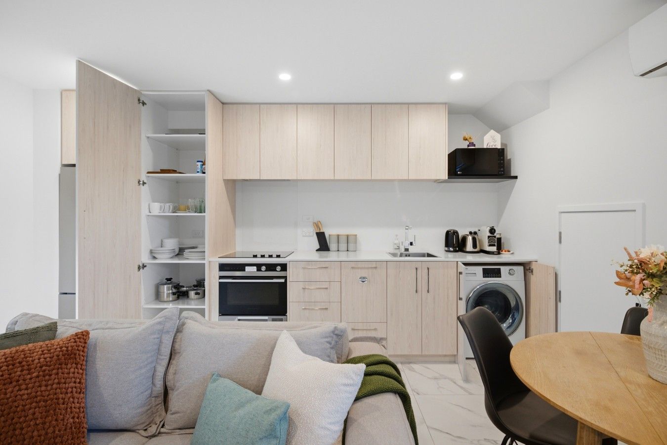 Een moderne keuken met inbouwapparatuur, een eethoek met een ronde tafel en een bank met kussens.