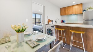 Ett modernt kök med träskåp, en tvättmaskin och en matplats med ett glasbord och barstolar.