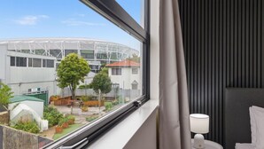 Ett hotellrum med utsikt över en modern byggnad, en liten trädgård och ett fönster med gardiner.